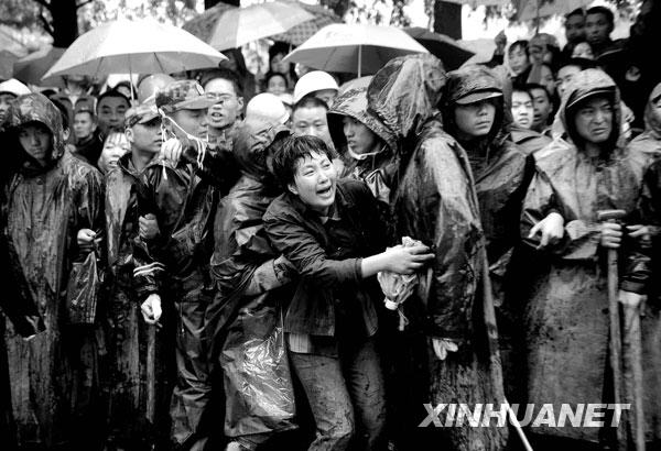 2008年5月13日，一名等待孩子消息的家长看到一名遇难学生的遗体被抬出后，奋力向前冲去。当天，救援人员继续在四川都江堰市聚源镇聚源中学冒雨进行救援工作。
